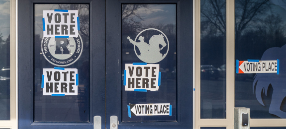 front doors to a polling station with 'Vote Here' sign taped to the front
