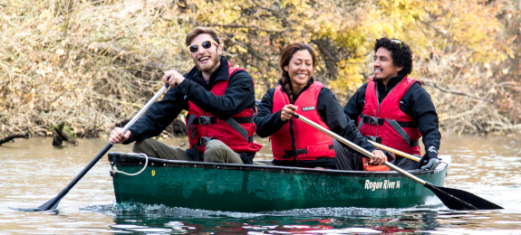 Two men and a woman smiling and paddling a green canoe