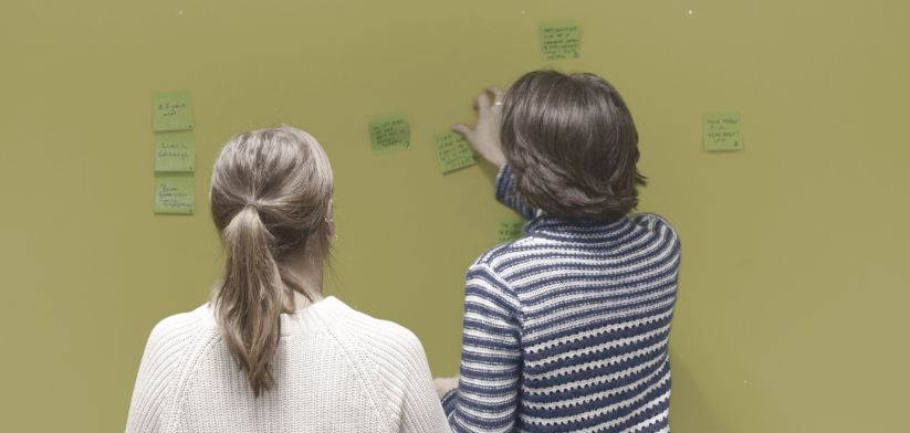 Two women placing post-it notes on the wall